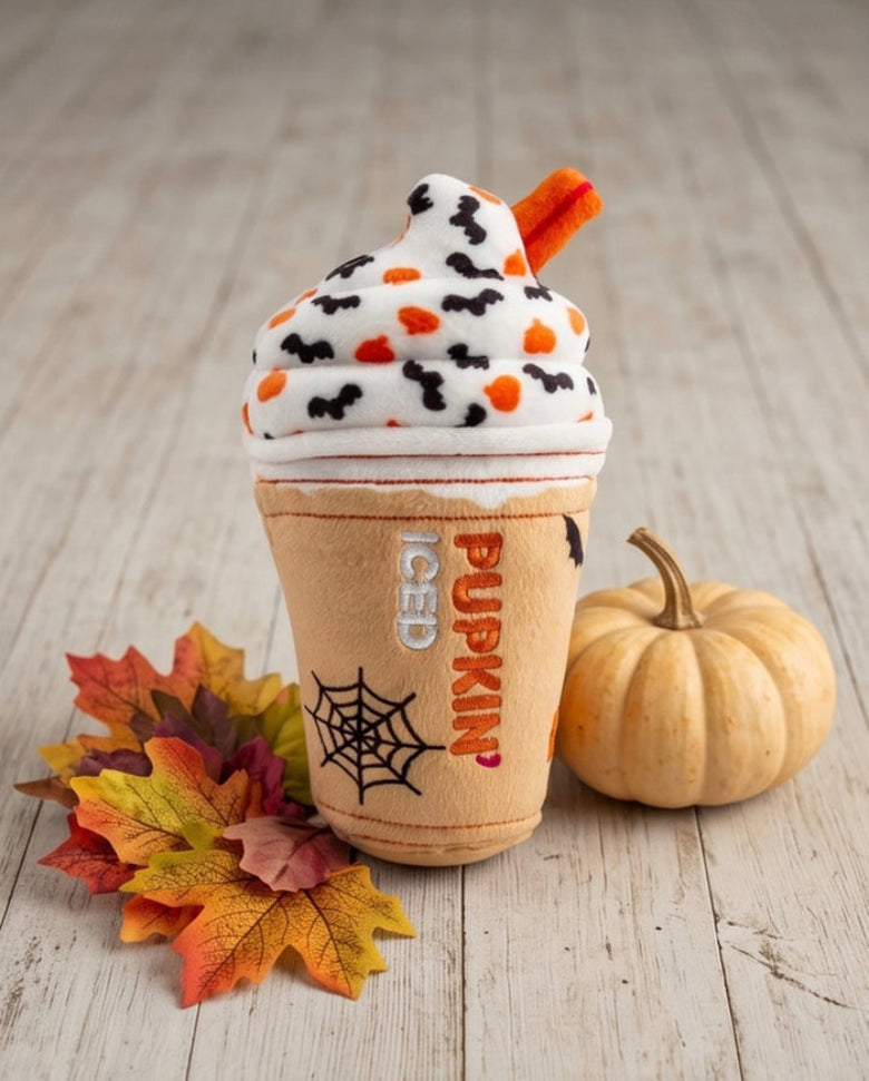Halloween-themed plush dog toy resembling a pumpkin spice latte on a wooden surface with leaves and a small pumpkin.